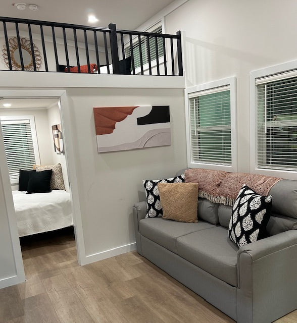 Living room with gray sofa, decorative pillows, and a view into a bedroom.